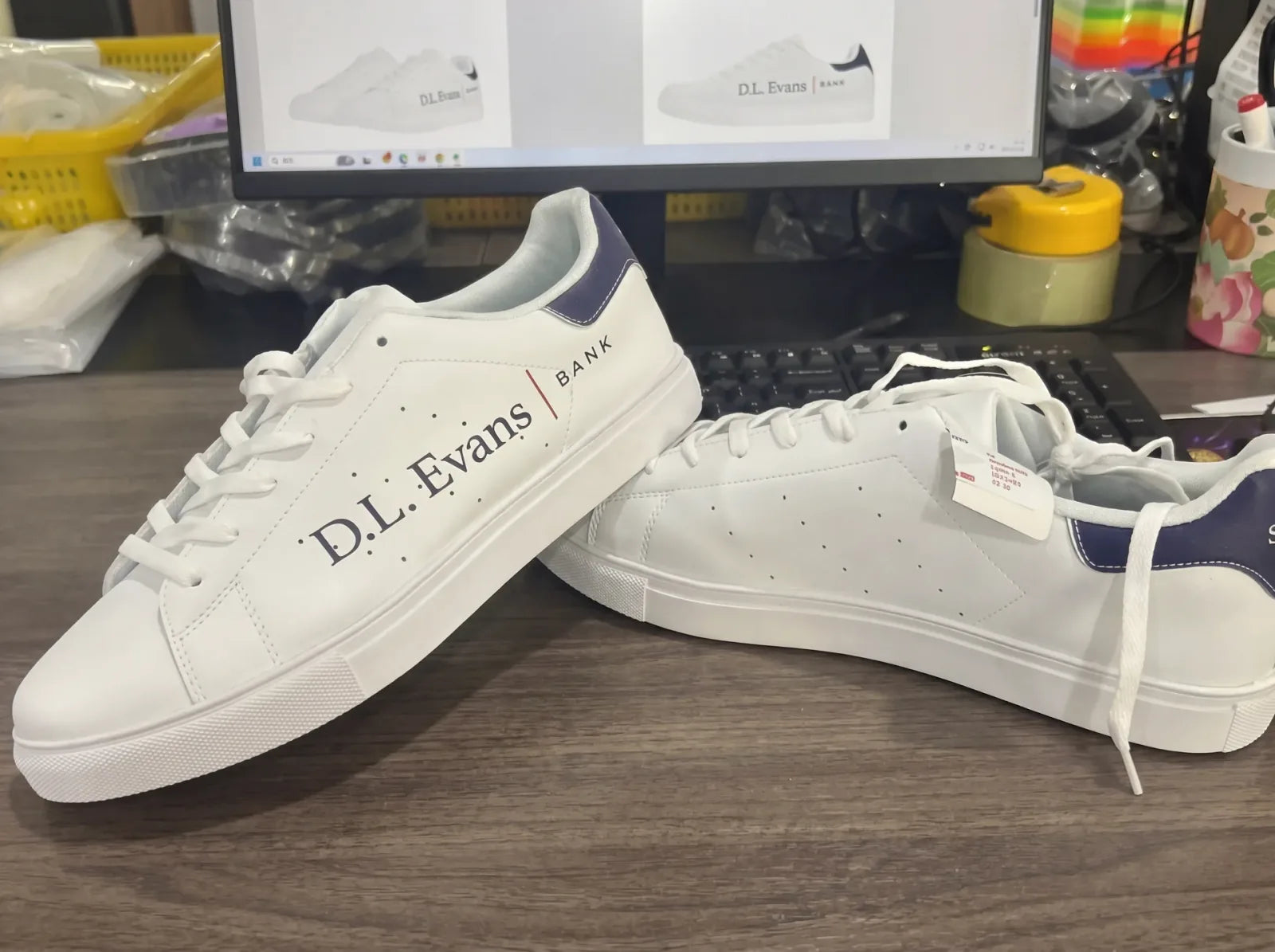 D.L. Evans Bank custom branded white sneakers with navy heel on desk in front of monitor showing the design mockup